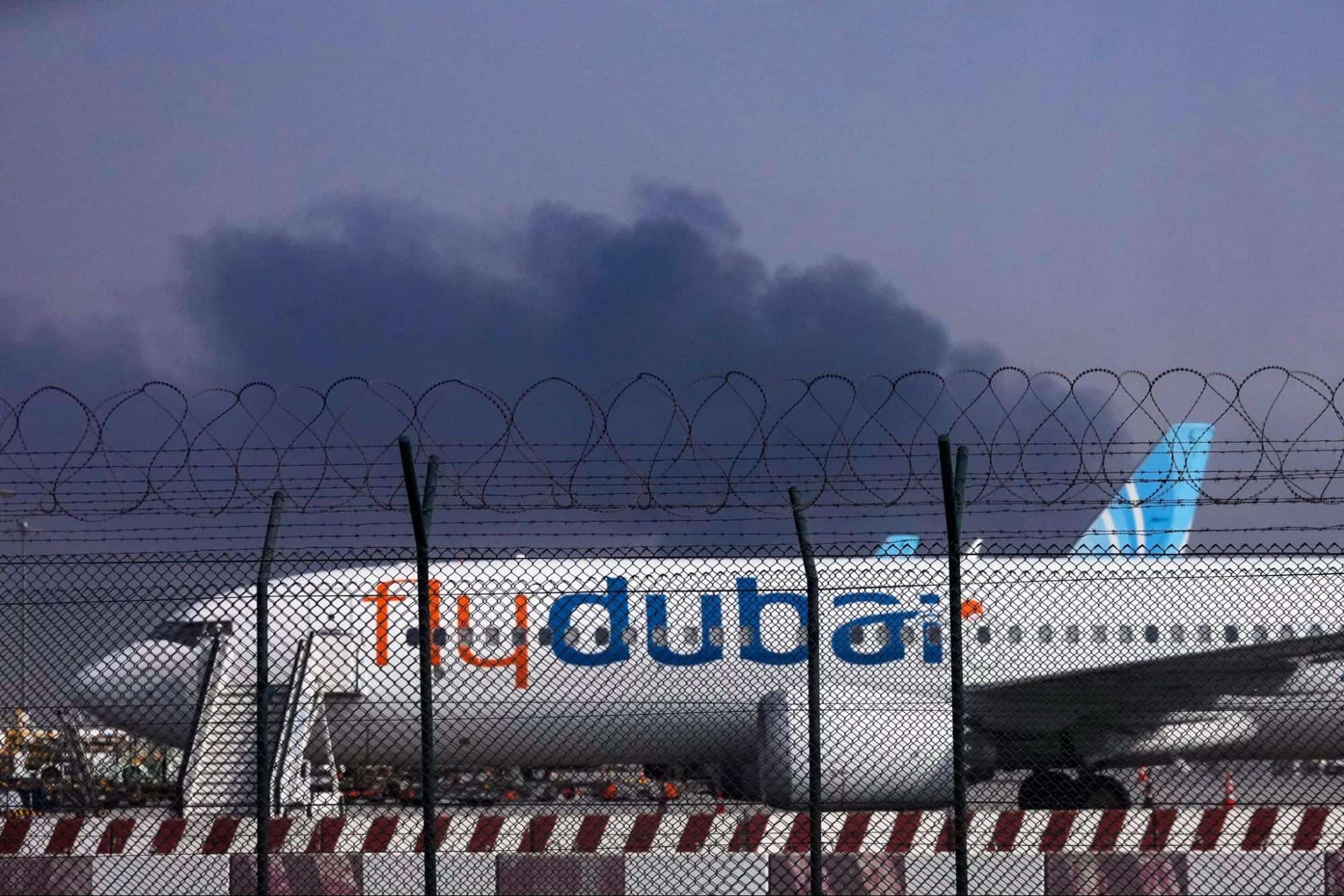 A FlyDubai plane is parked at Dubai International Airport as smoke rises in the background after a drone struck a fuel tank early morning, forcing the temporary suspension of flights, in Dubai, United Arab Emirates, Monday, March 16, 2026. (AP Photo)