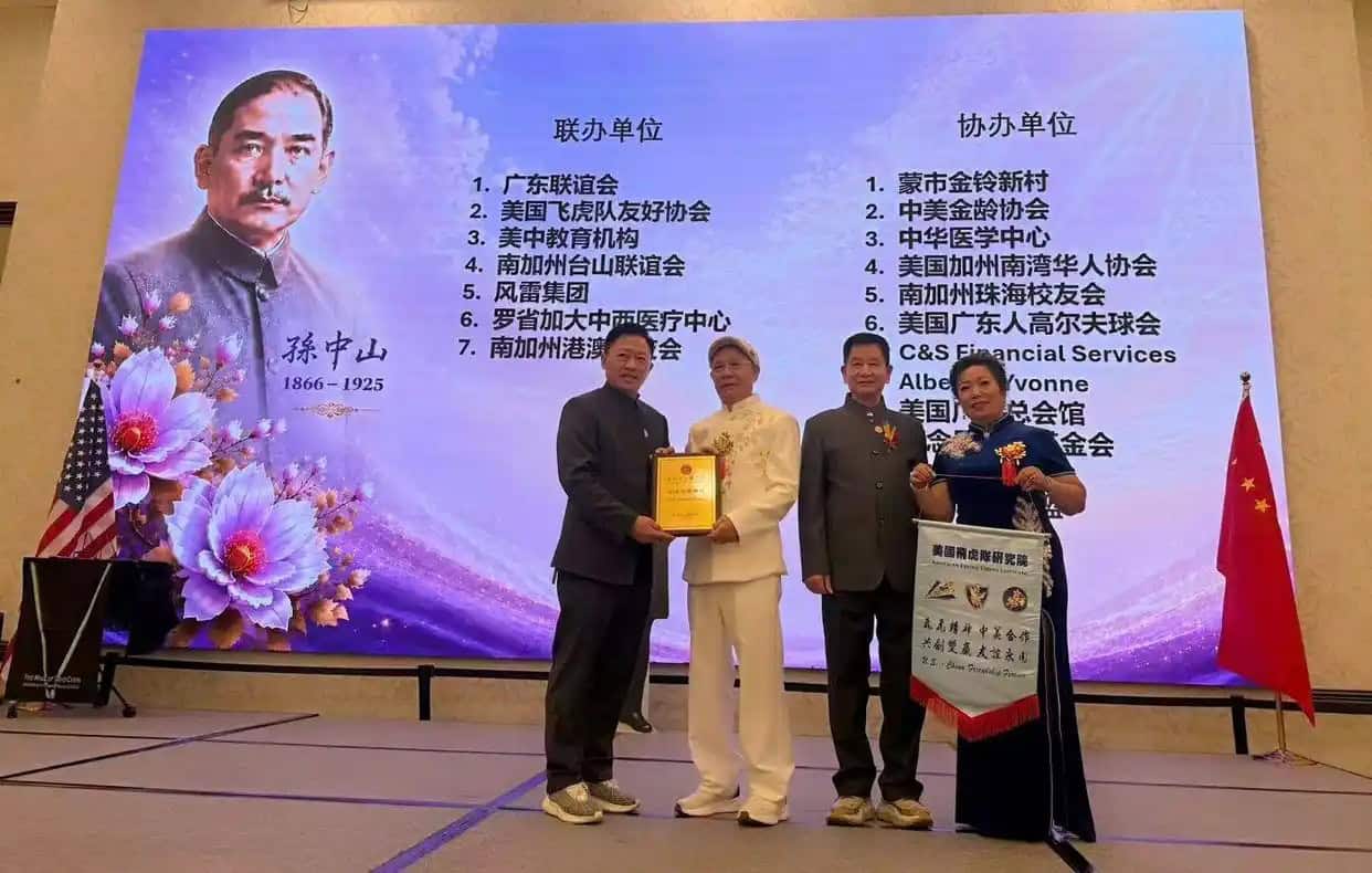 洛城中山聯誼會為美國飛虎隊研究院院長陳燦培(左二)頒發榮譽會長。背後的投影幕展示了該活動的聯辦與協辦單位。(圖片來源:百度)